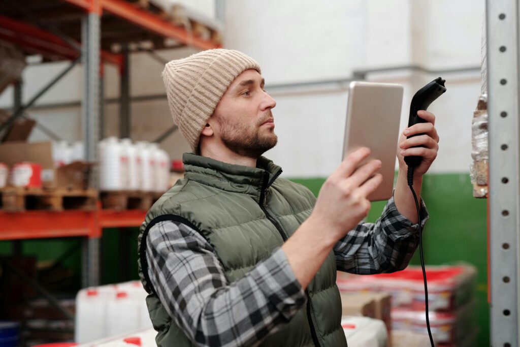 pexels-photo-4483941-4483941 Man in beanie and vest using a scanner in a warehouse for inventory control.